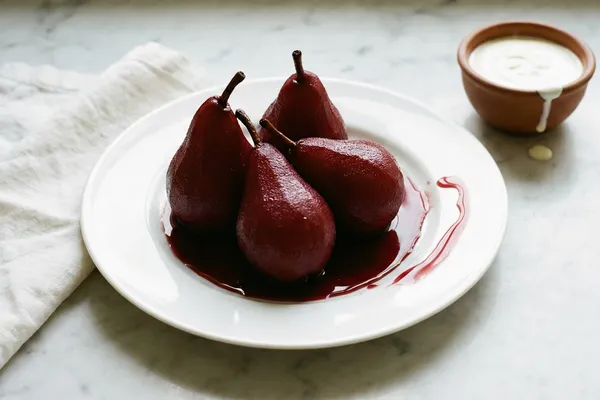 Deep crimson poached pears glistening with wine syrup on a white porcelain plate with a bowl of crème fraîche