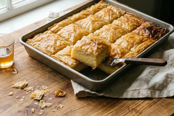Diamond-cut golden phyllo pastry with creamy custard filling in a baking pan on olive wood