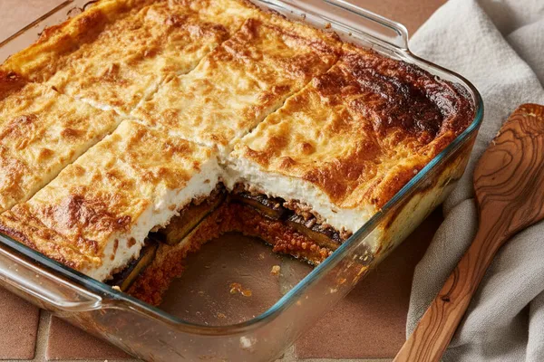 Golden-topped layered casserole in a baking dish with a portion cut showing eggplant and meat layers